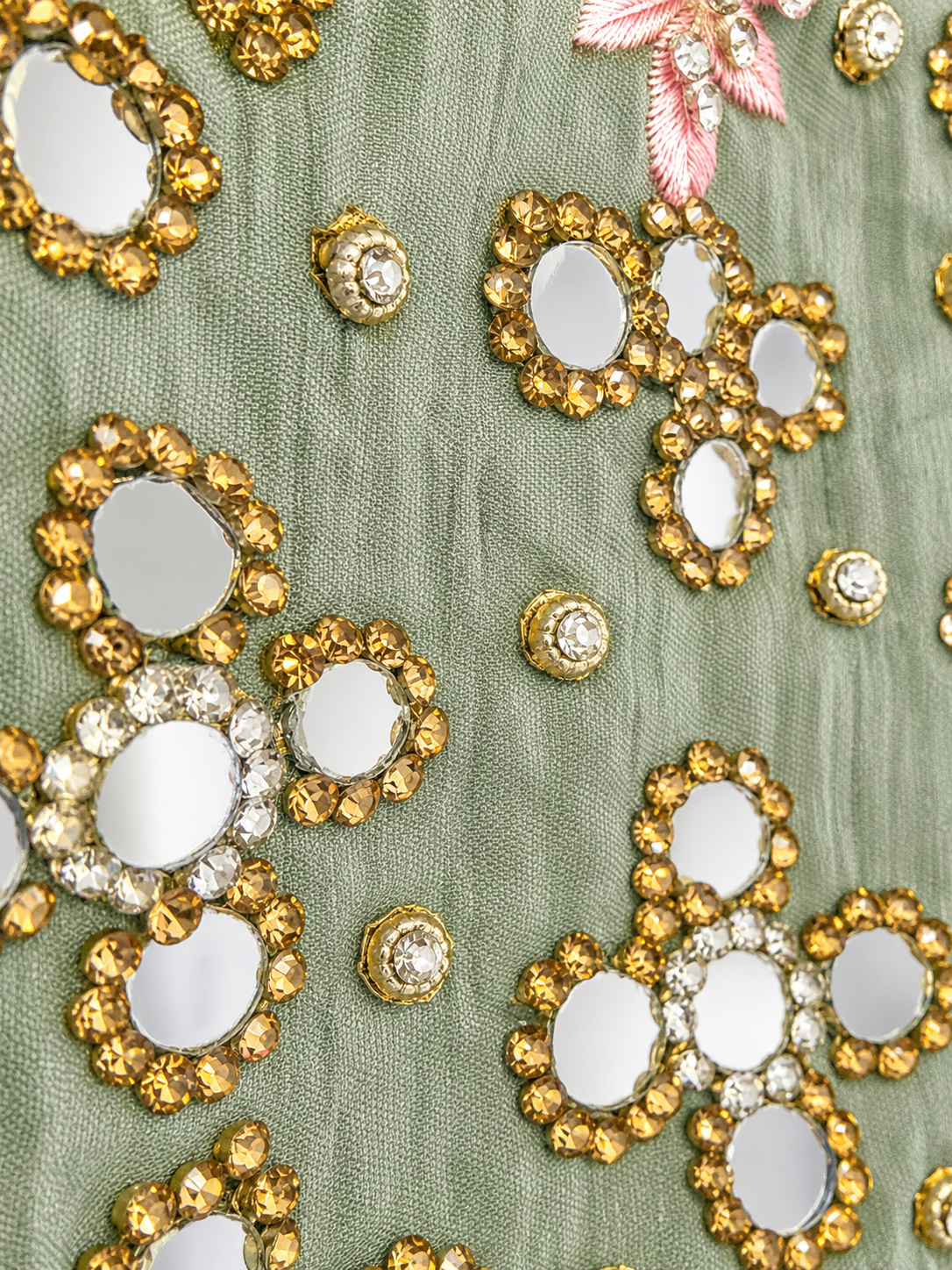 Close-up of sage green fabric with mirrorwork and pink embroidery